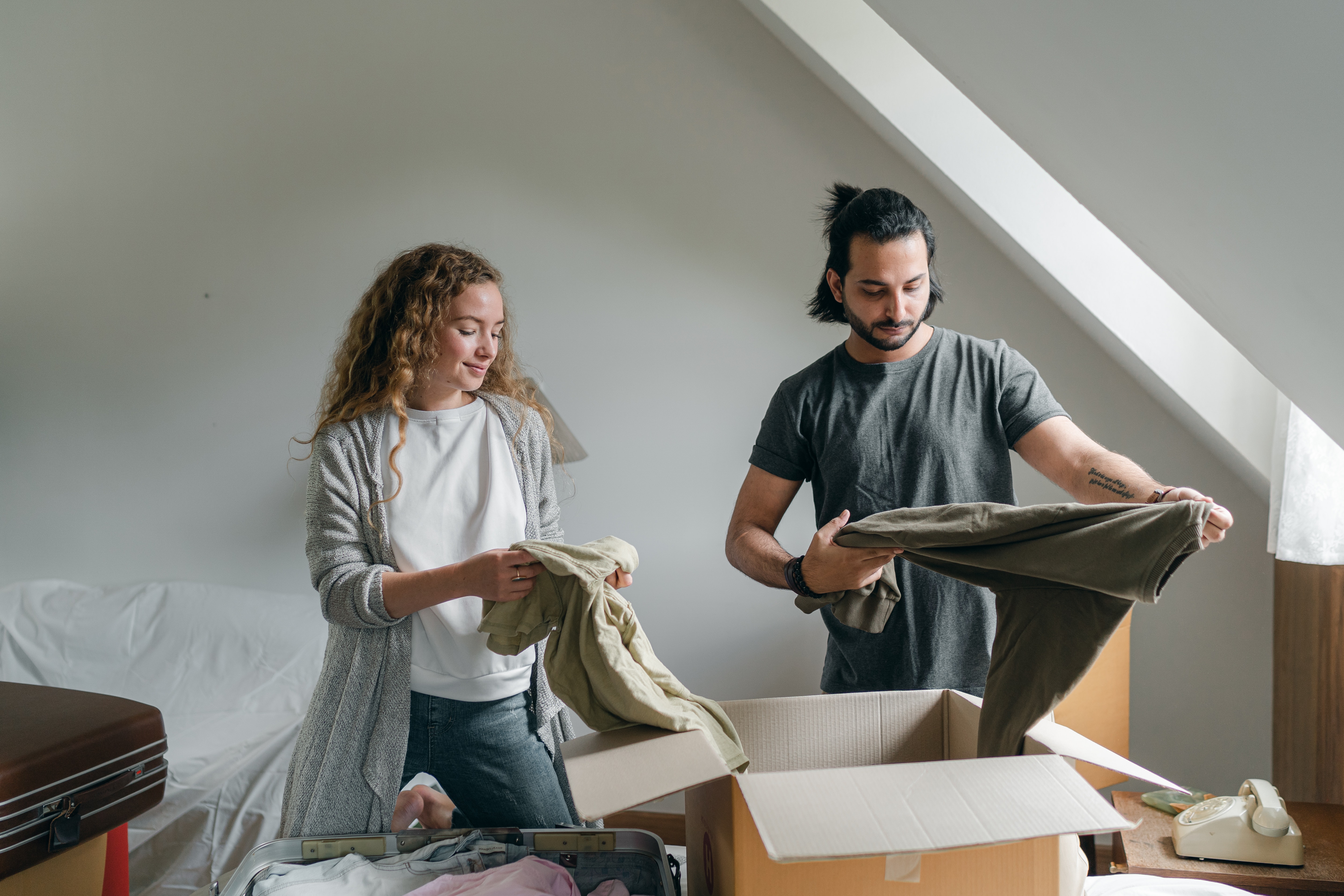 two young people dressed casually folding clothes and packing them in moving boxes