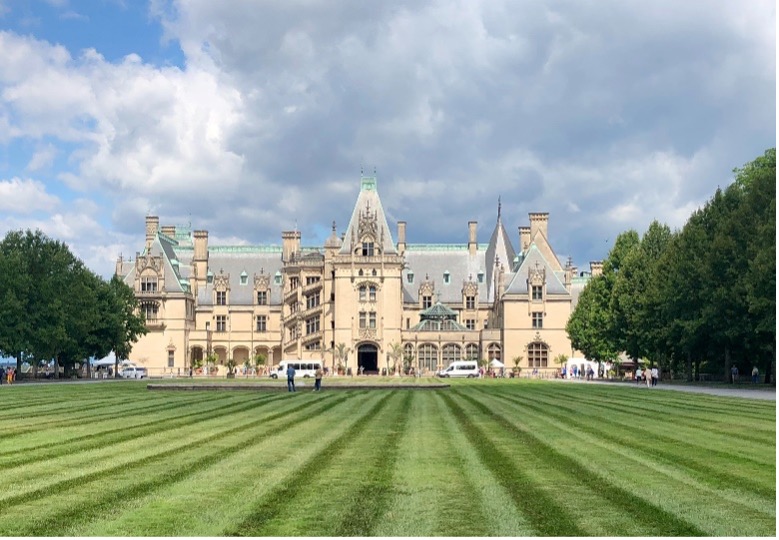 The ornate Biltmore Estate sits tall beneath a blue sky surrounded by trees