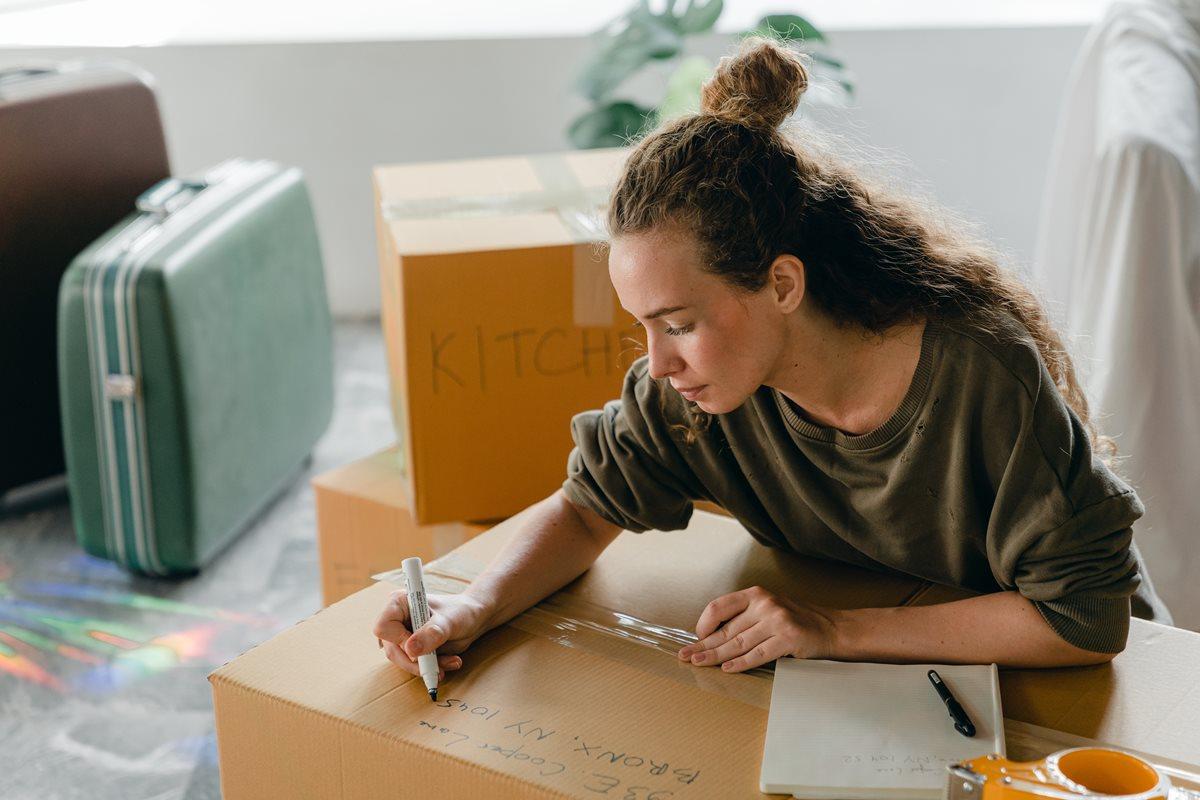 young woman with long curly hair labeling a moving box with its contents before moving day