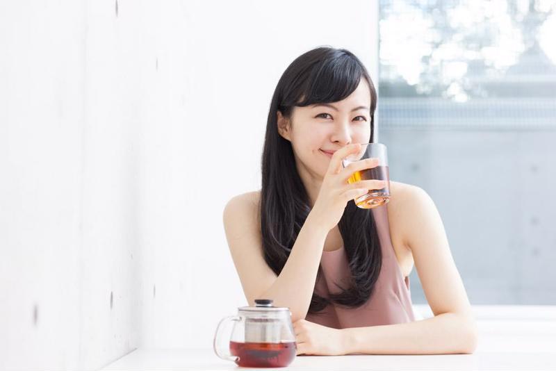 A woman enjoying a glass of juice at her kitchen table.