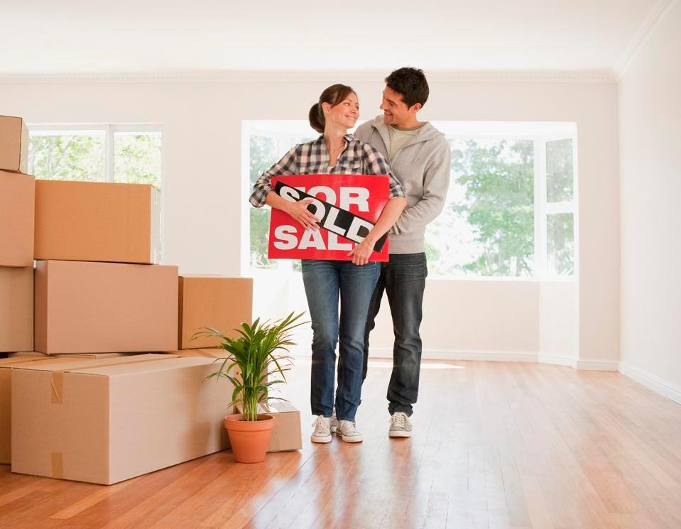 Couple holding a sold sign in a house full of boxes