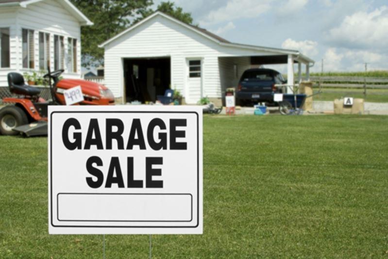 A yard with a garage sale sign stuck in it. 
