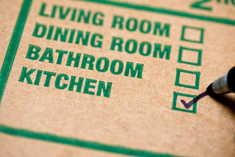 Box label noting whether the container belongs in the living room, dining room, bathroom or kitchen with the latter marked.