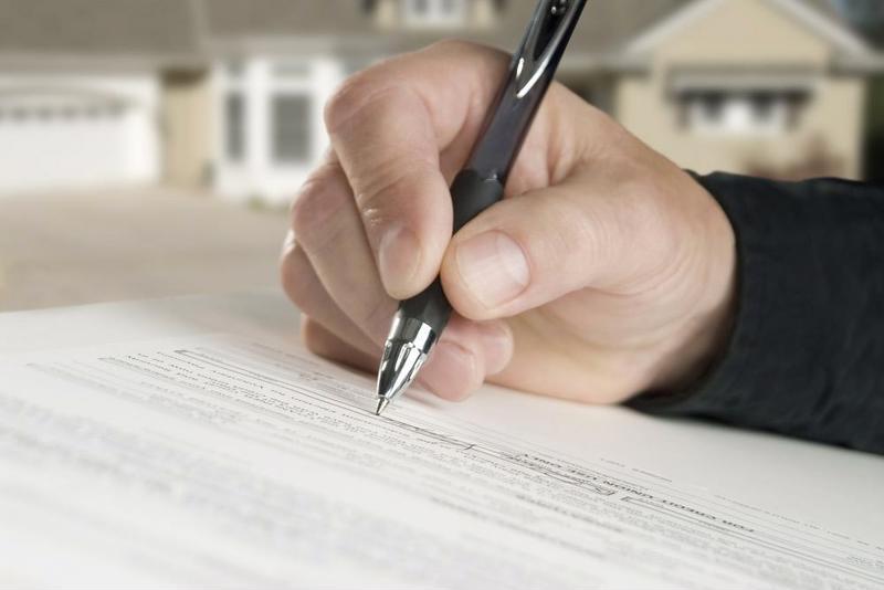 A close up of a person's hand signing a home insurance policy.