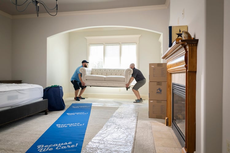 Atlas team members carefully moving couch inside a home interior.
